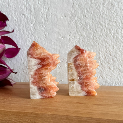 Two dogtooth crystal towers on a wooden surface with a white wall background