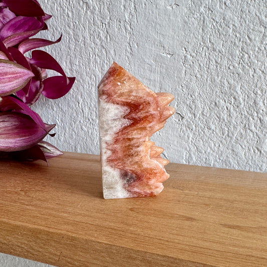 Dogtooth calcite crystal on a wooden surface with a white wall and purple flowers in the background