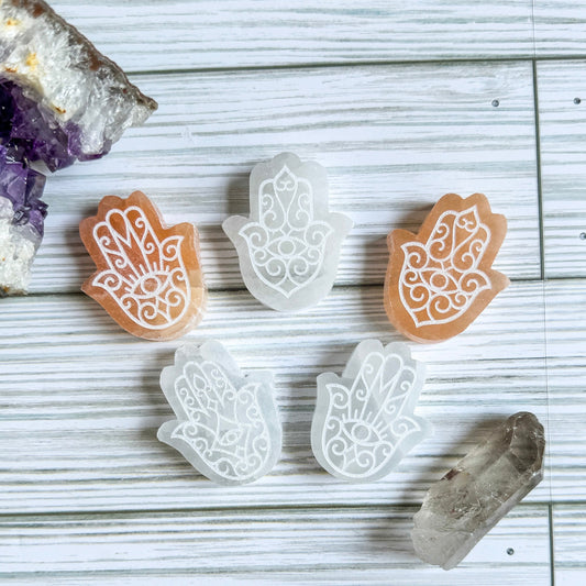 Five engraved Hamsa hand-shaped carvings on a wooden surface with crystals.