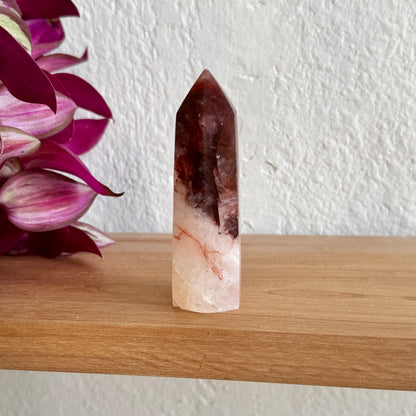 Hematoid crystal tower on a wooden surface with a white wall and purple flowers in the background
