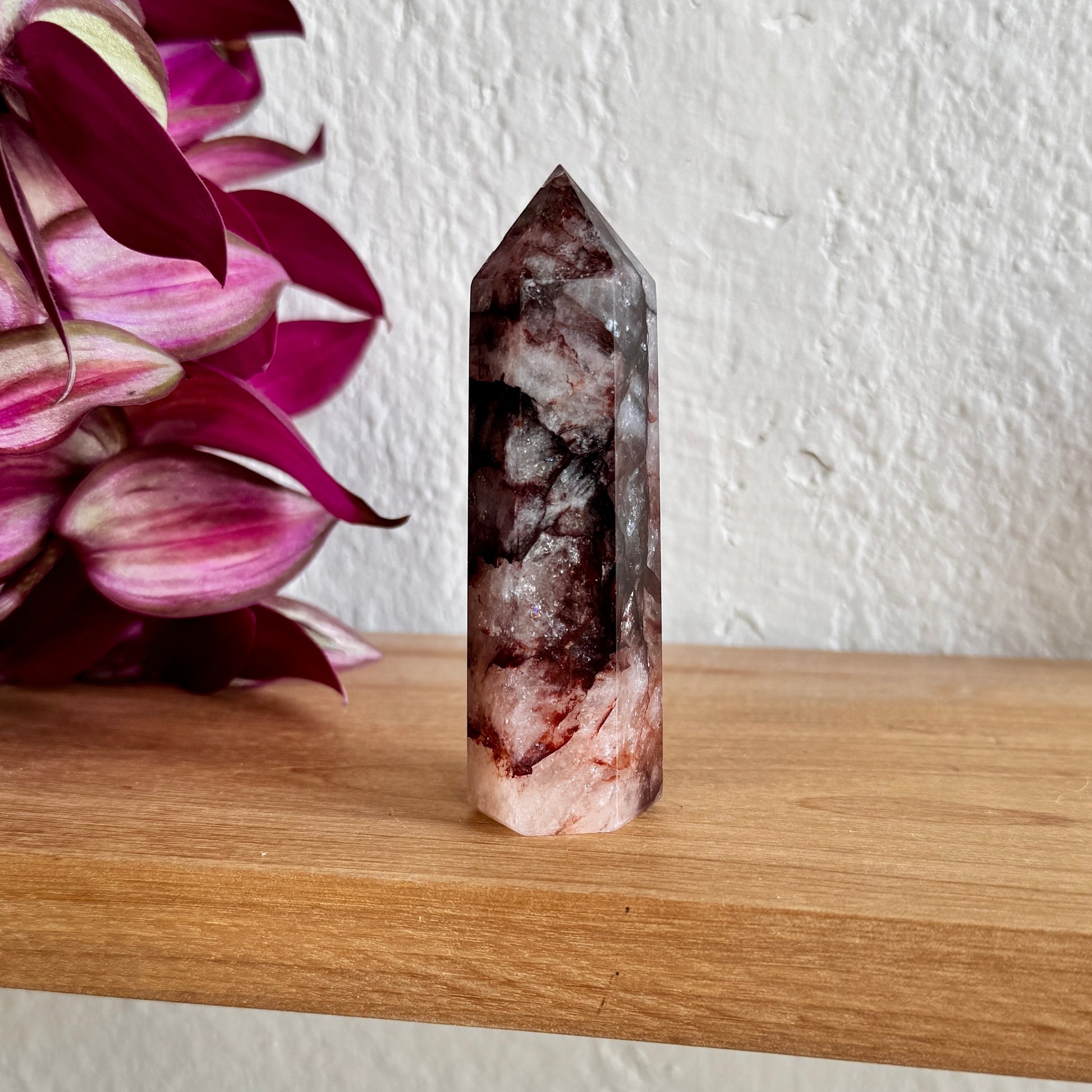 Fire quartz tower on a wooden surface with a white wall and pink flowers in the background