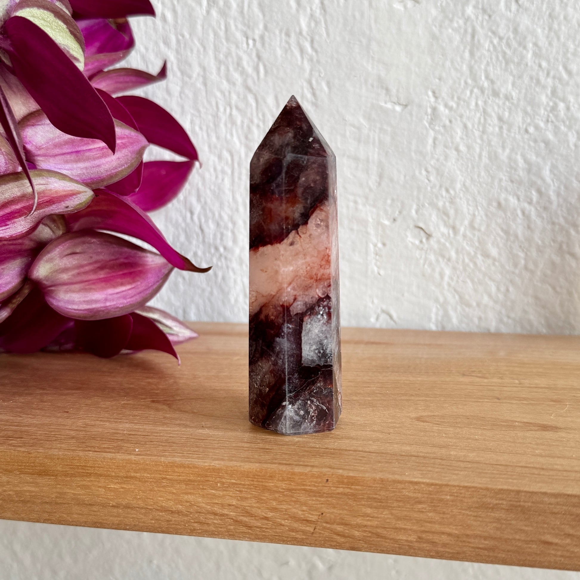 Fire quartz tower on a wooden surface with a white wall and pink flowers in the background