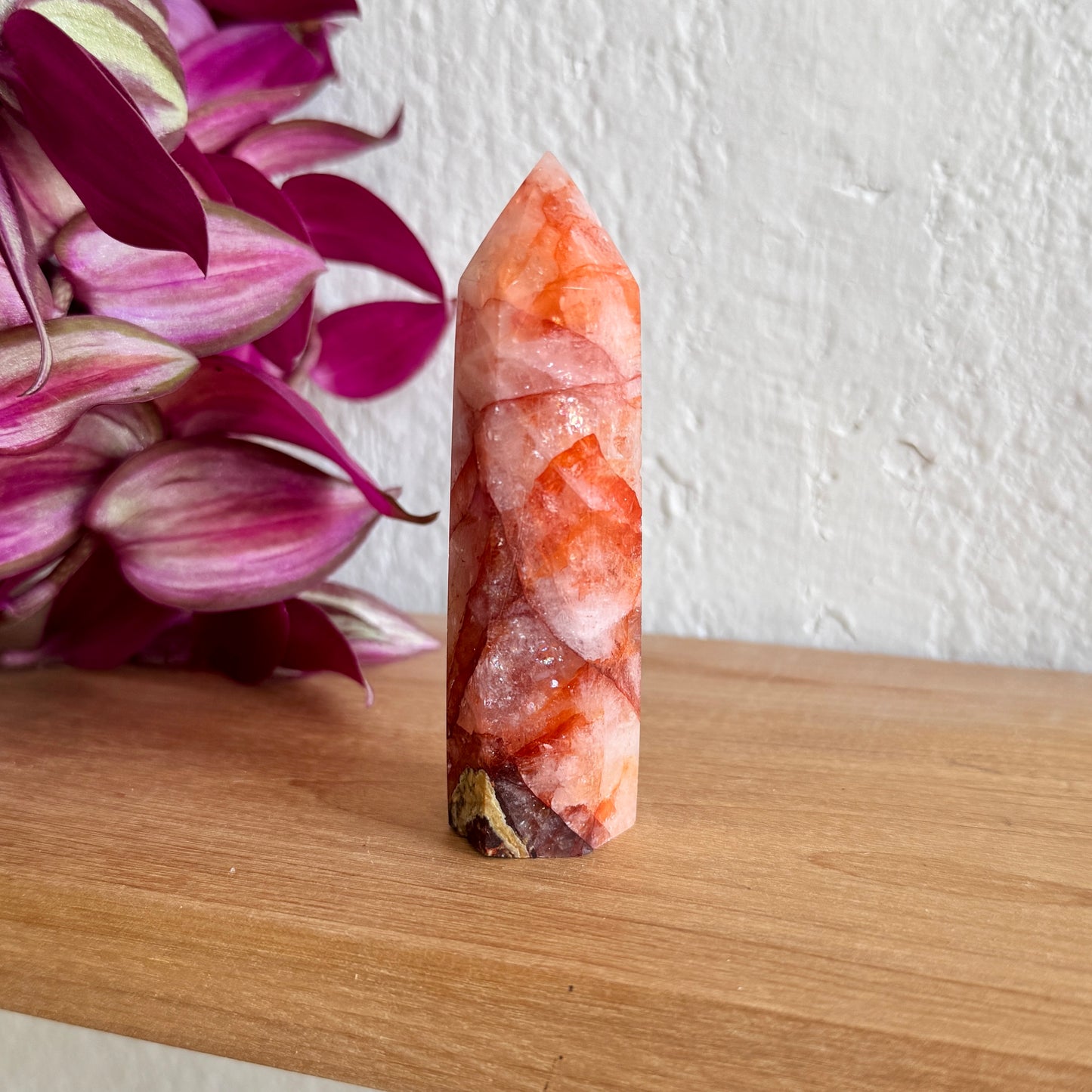 Decorative fire quartz crystal tower on a wooden surface with pink flowers in the background