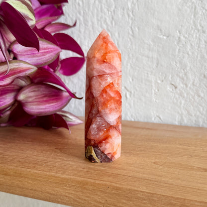 Decorative fire quartz crystal tower on a wooden surface with pink flowers in the background