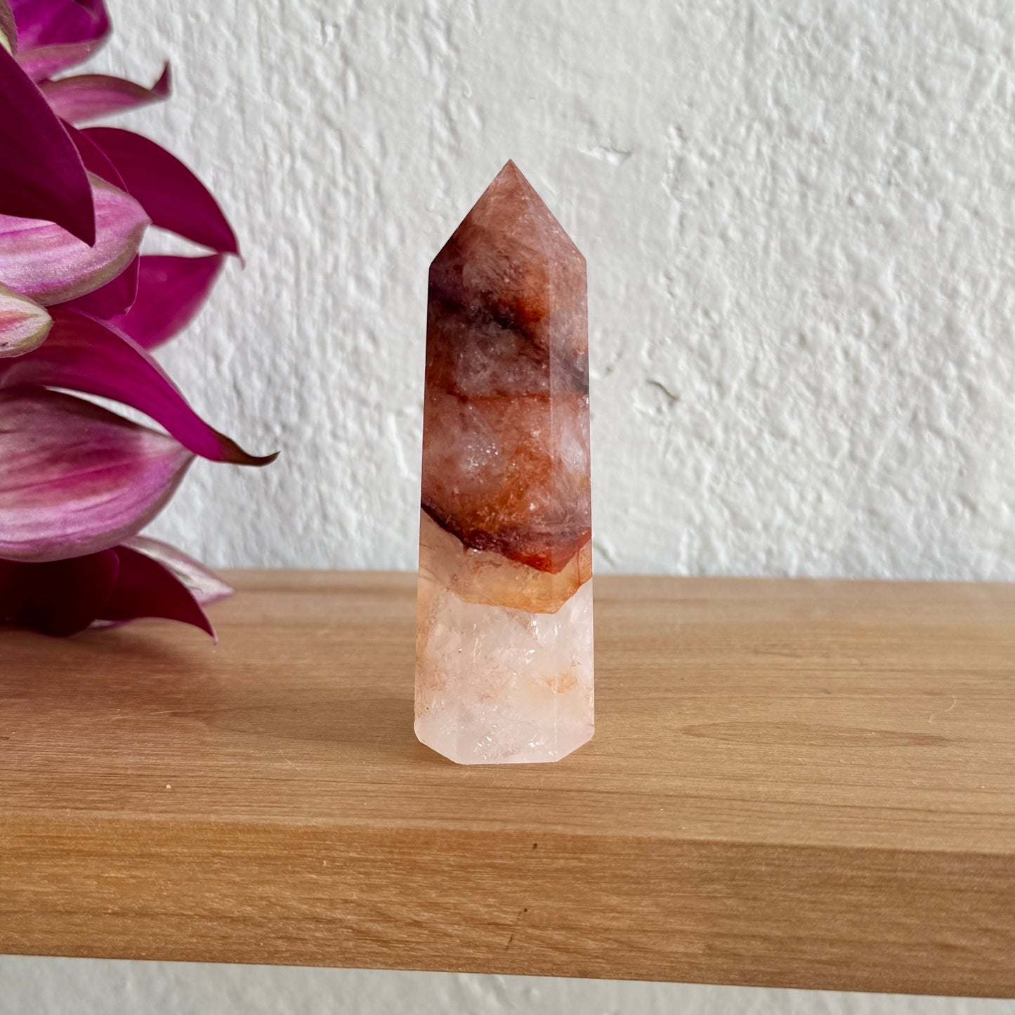 Fire quartz crystal tower on a wooden surface with a white wall and purple flower in the background