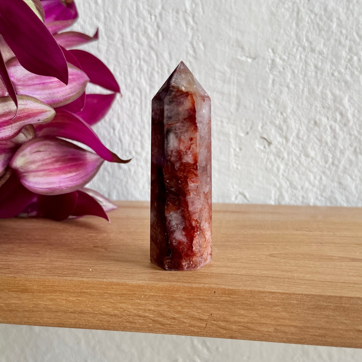 Fire quartz tower on a wooden surface with pink flowers in the background