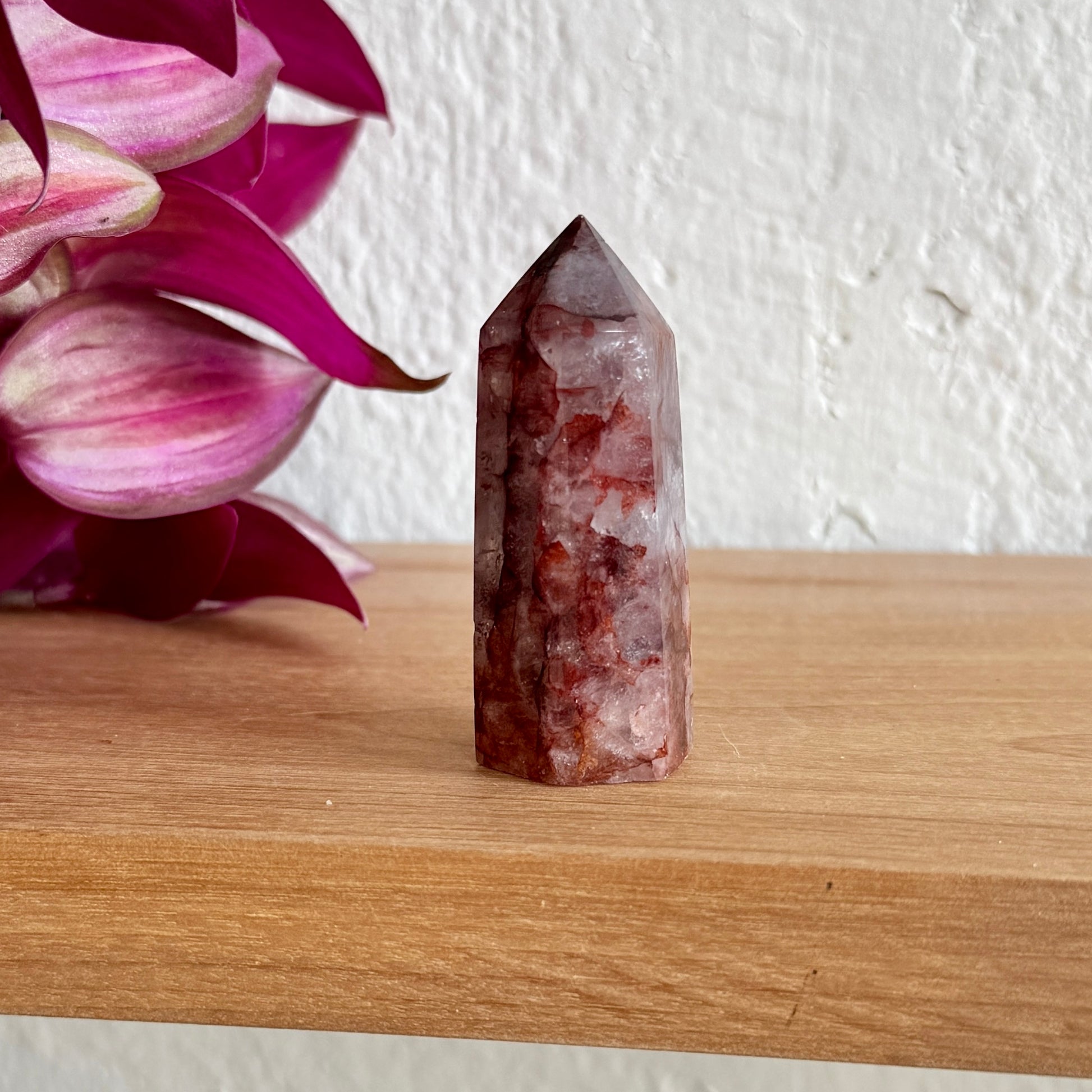 Hematoid quartz crystal tower on a wooden surface with pink flowers in the background