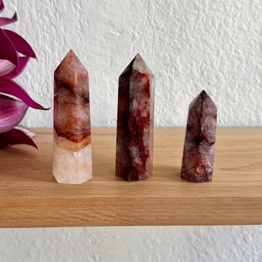 Three hematoid quartz crystal towers on a wooden surface with a white wall background