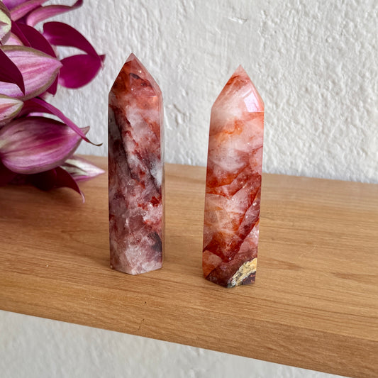 Two fire quartz red crystal towers on a wooden surface with a white wall background