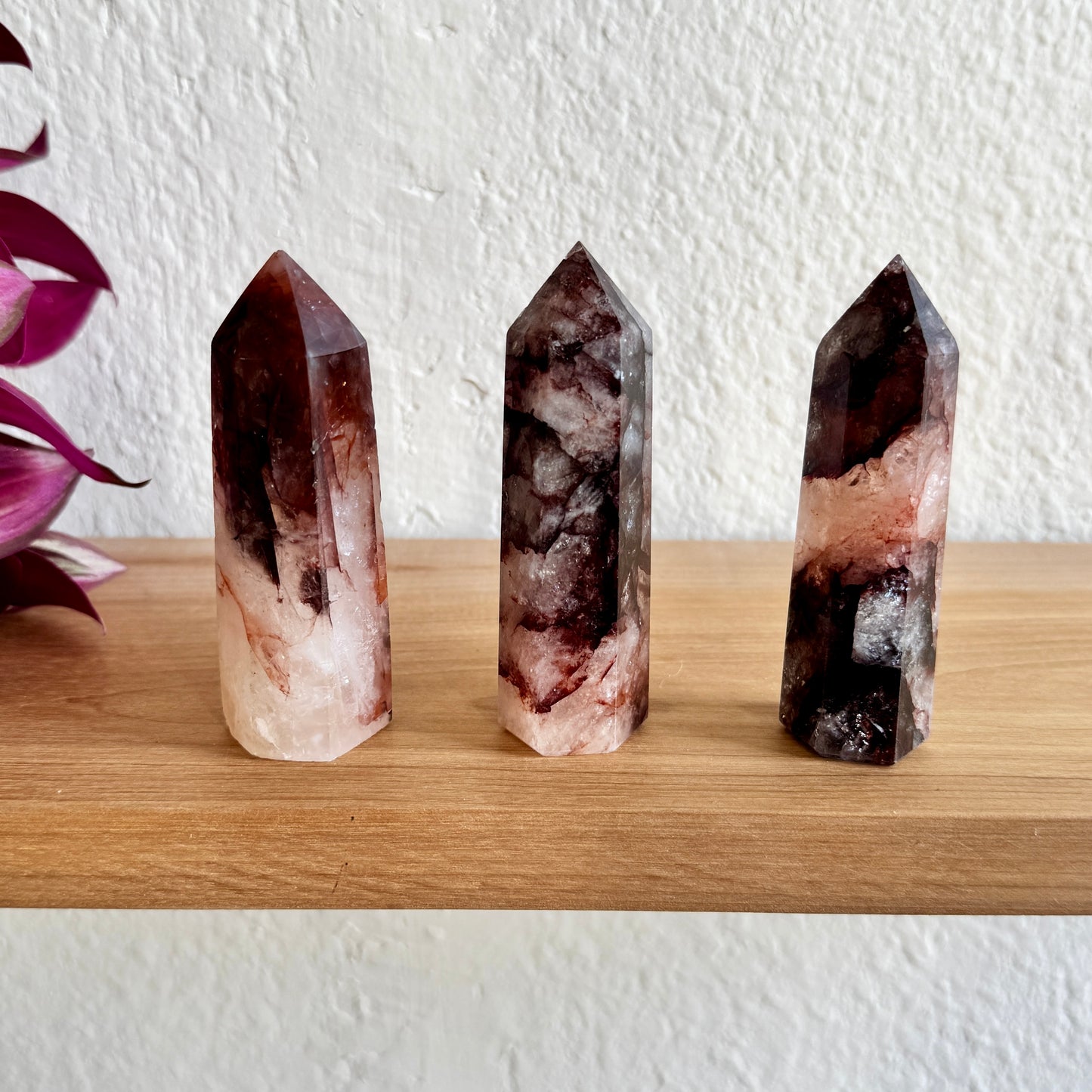Three fire quartz crystal points on a wooden surface with a white wall background