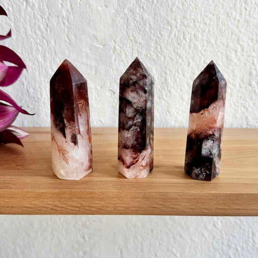 Three fire quartz crystal points on a wooden surface with a white wall background