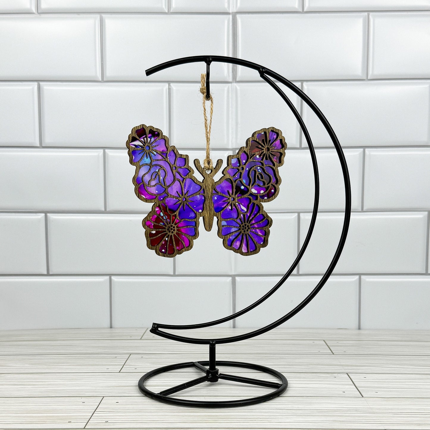Floral butterfly suncatcher made from wood and acrylic shown in dark stain option hanging on a metal stand in front of a white tiled wall.
