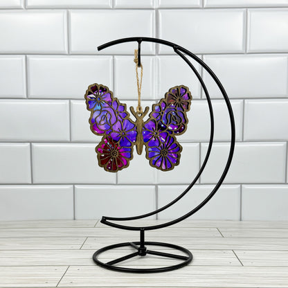 Floral butterfly suncatcher made from wood and acrylic shown in dark stain option hanging on a metal stand in front of a white tiled wall.