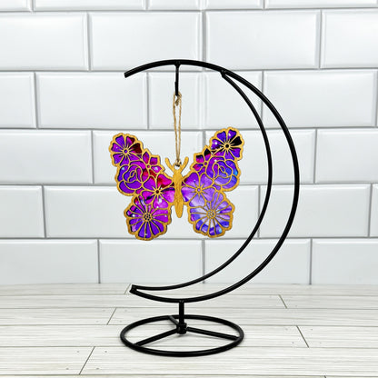 Floral butterfly suncatcher made from wood and acrylic shown in light stain option hanging on a metal stand in front of a white tiled wall.