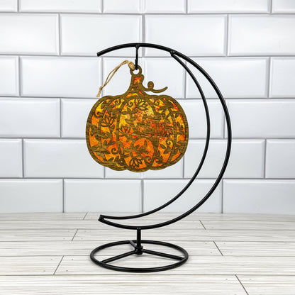 Floral Pumpkin suncatcher made from wood and acrylic hanging on a metal stand in front of a white tiled wall.