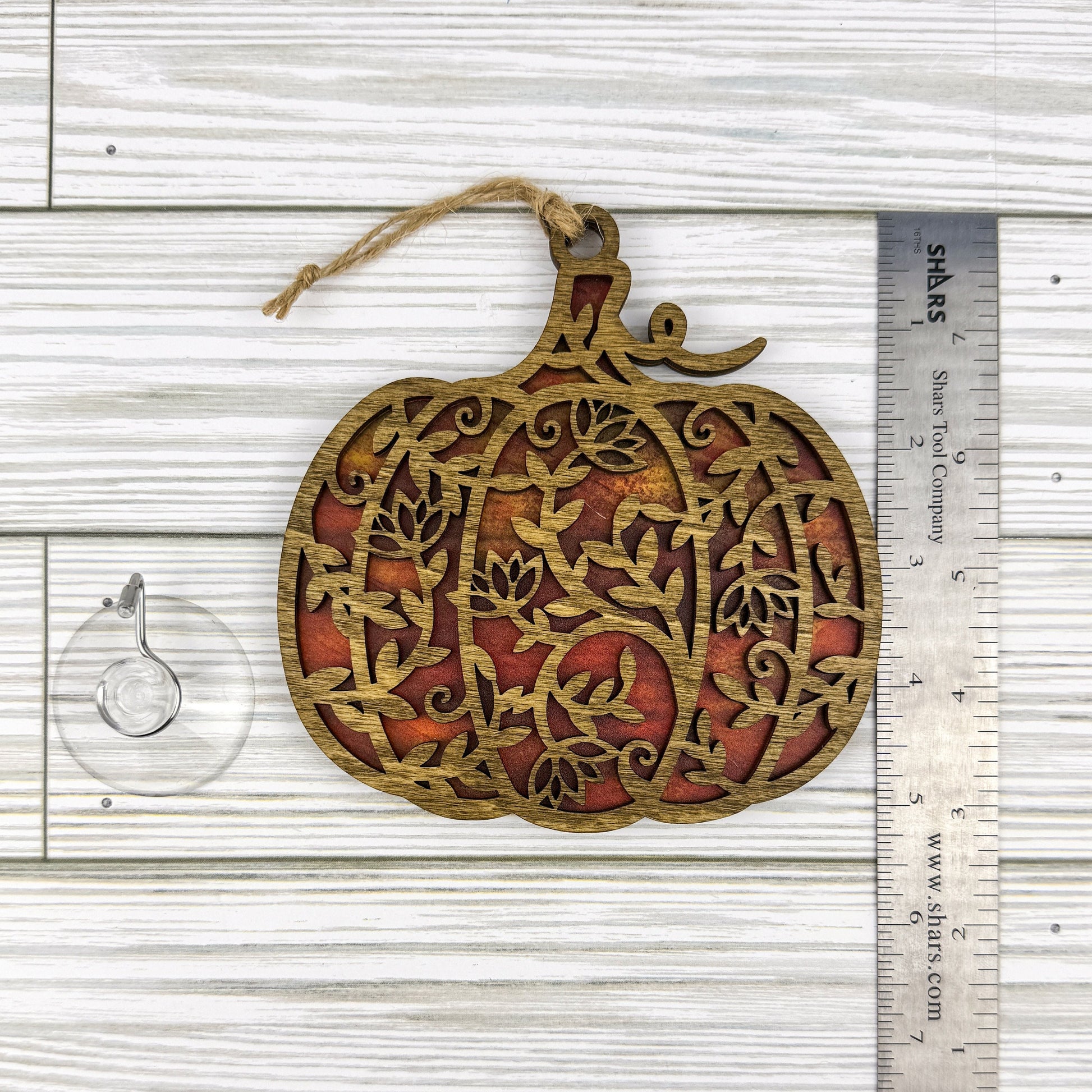 Floral pumpkin suncatcher made from wood and acrylic lying flat with a ruler showing the approximate height.
