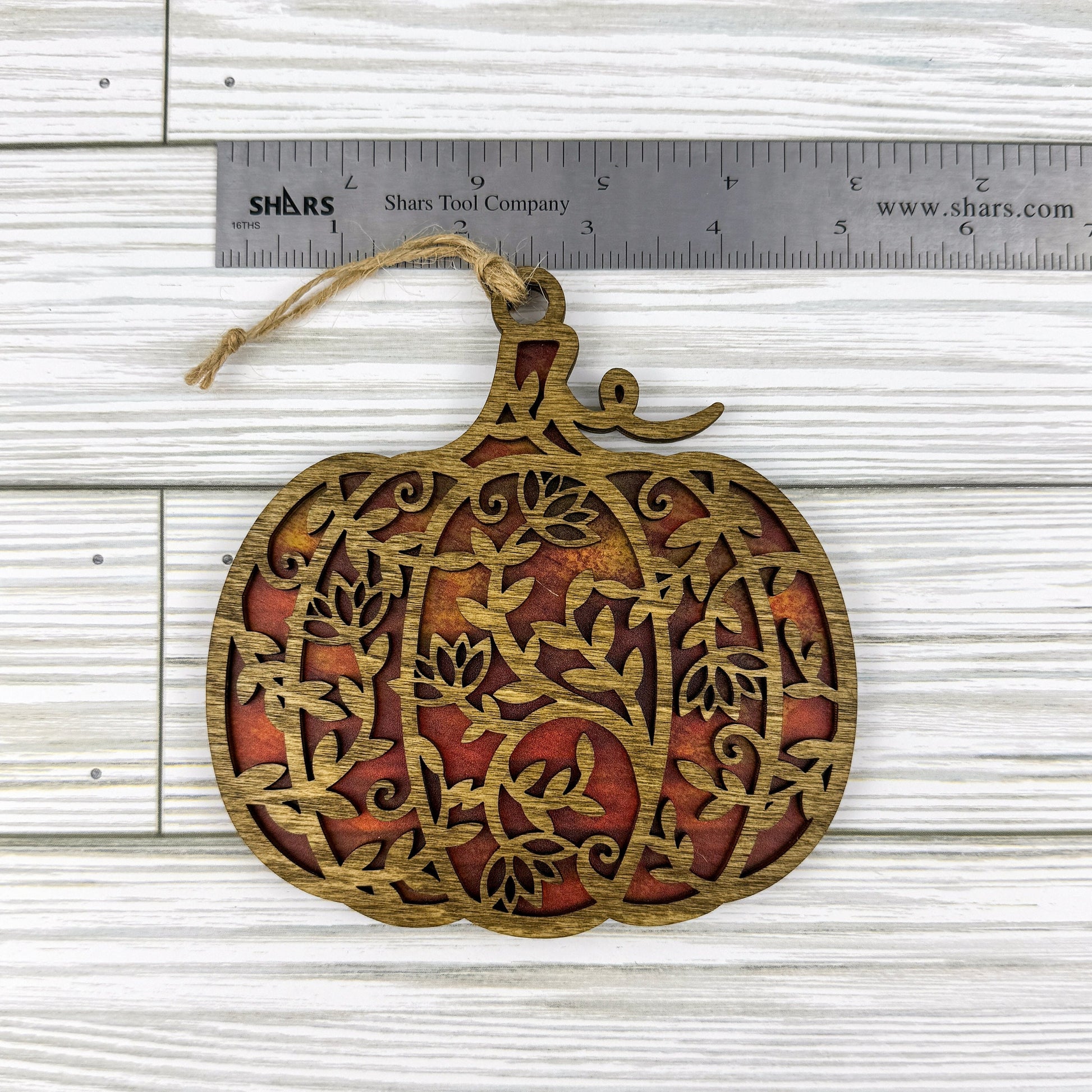 Floral pumpkin suncatcher made from wood and acrylic lying flat with a ruler showing the approximate width.