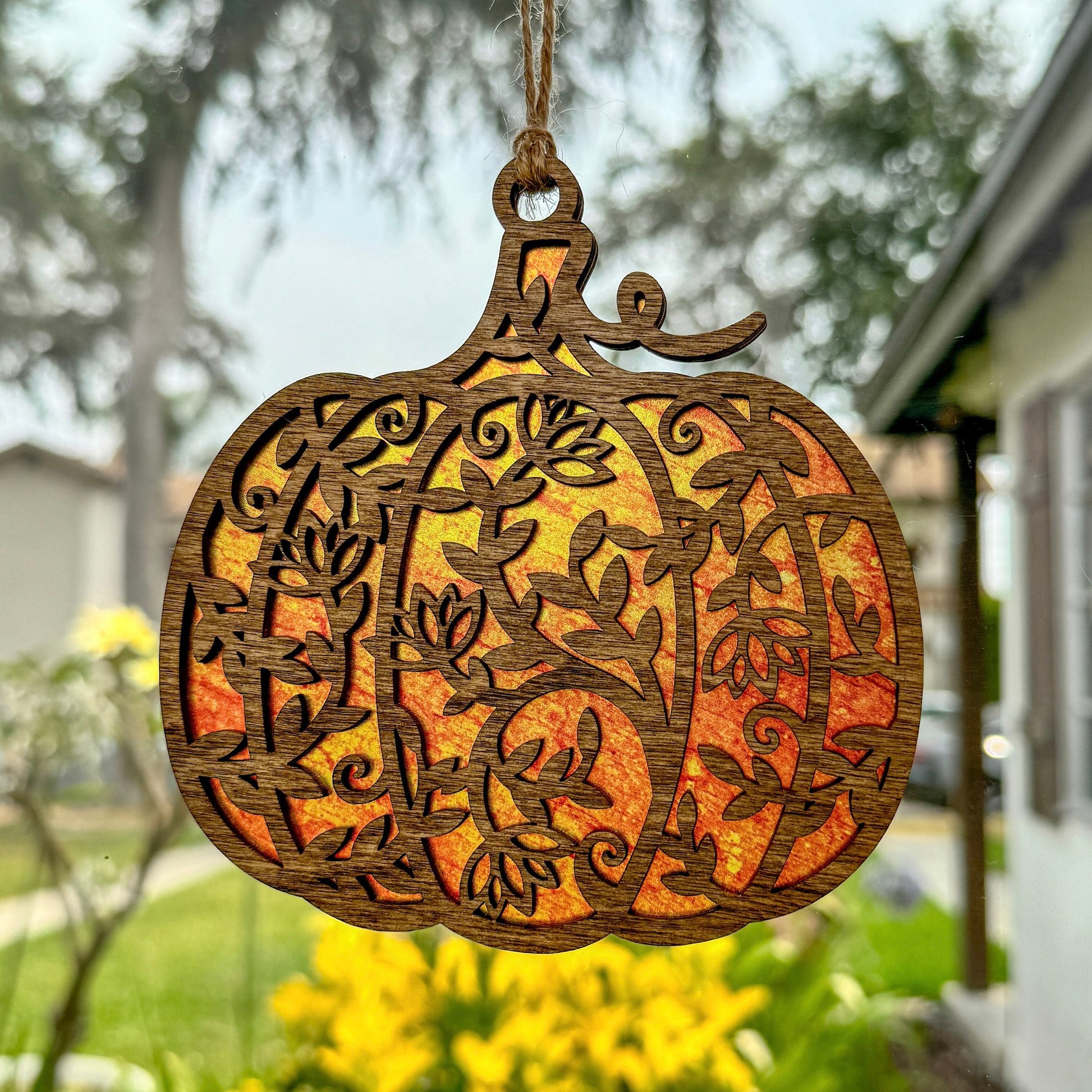Floral pumpkin suncatcher made from wood and acrylic hanging in window.