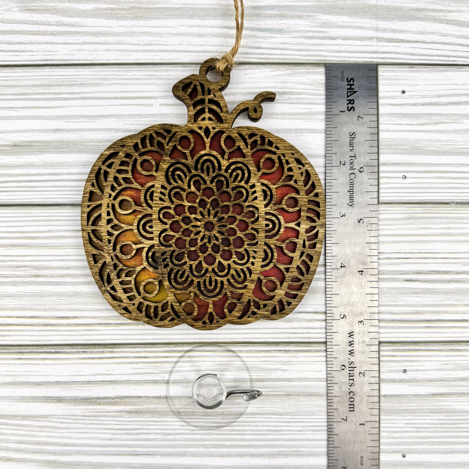 Geometric pumpkin suncatcher made from wood and acrylic lying flat with a ruler showing the approximate height.