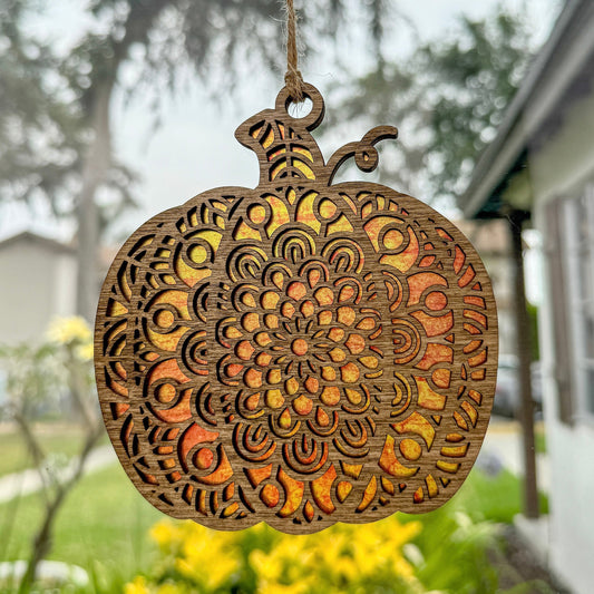 Geometric pumpkin suncatcher made from wood and acrylic hanging in window.