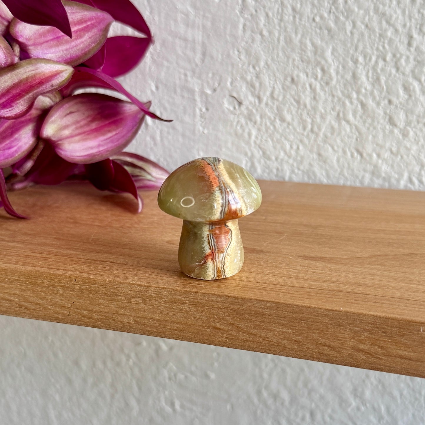 Decorative calcite stone mushroom on a wooden surface with pink flowers in the background