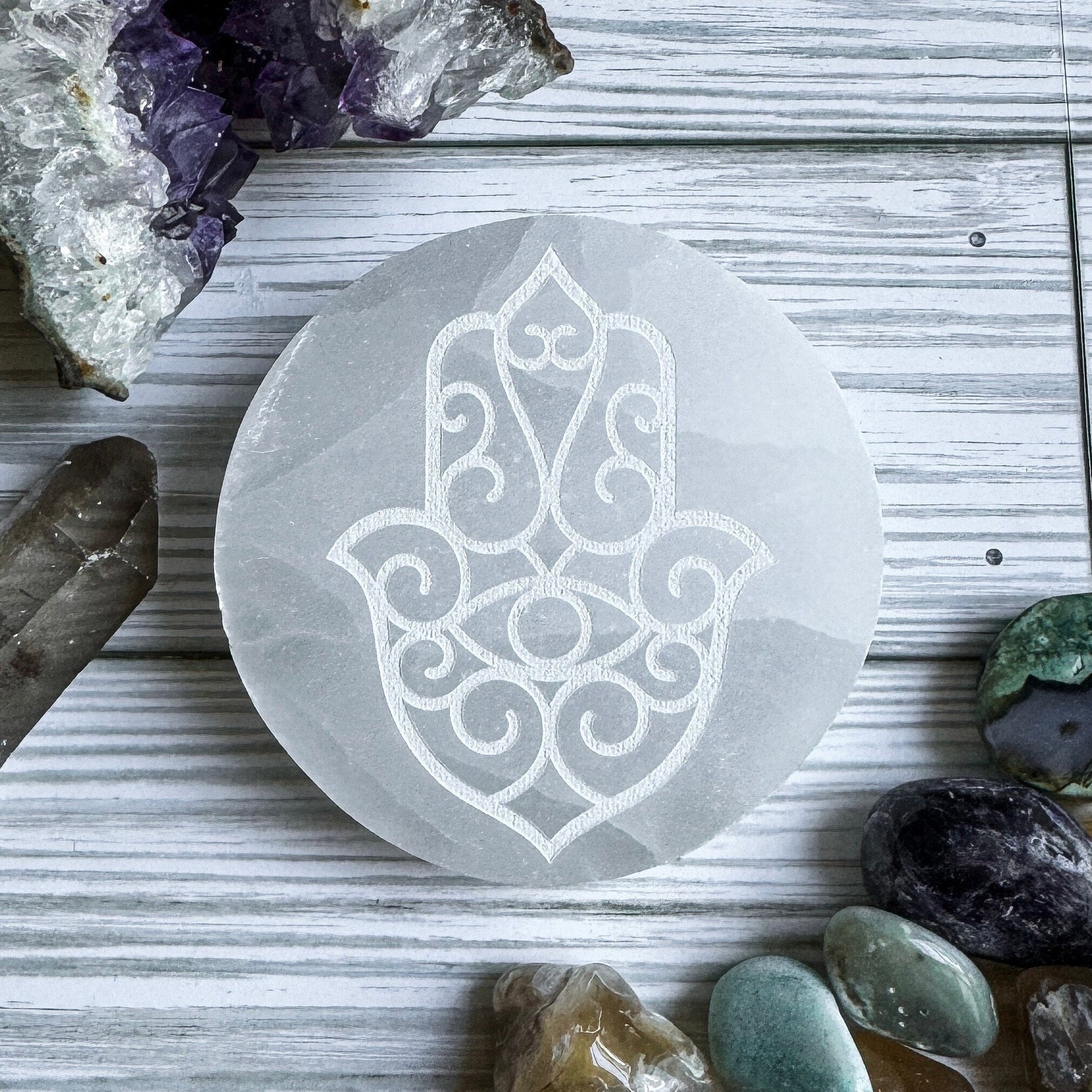 Selenite charging plate with Hamsa design on a wooden surface