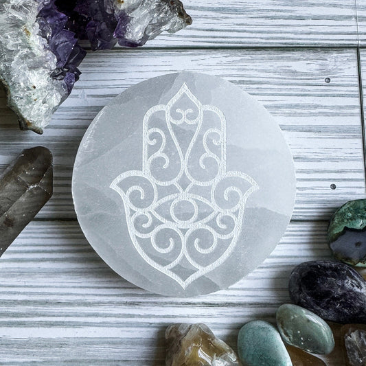 Selenite charging plate with Hamsa design on a wooden surface