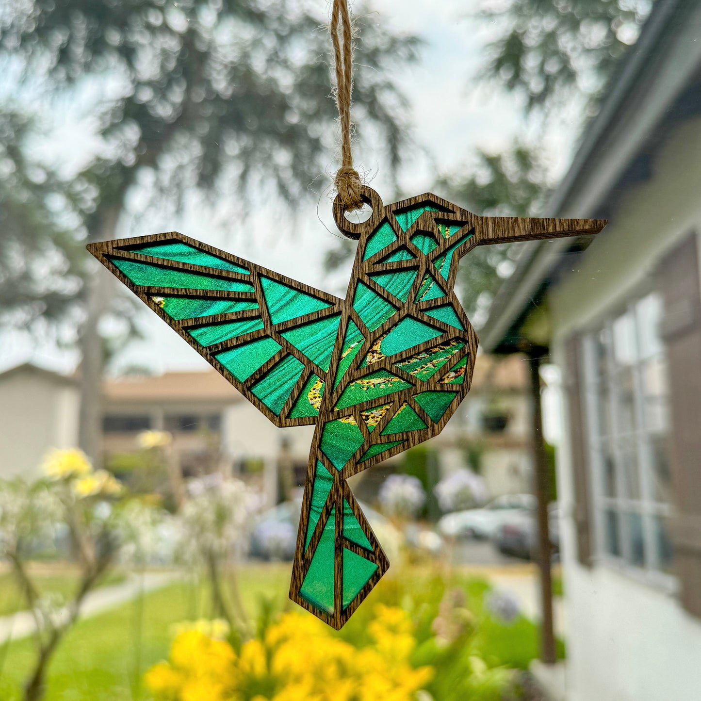 Geometric hummingbird suncatcher made from wood and acrylic hanging in window shown in the dark stain option.
