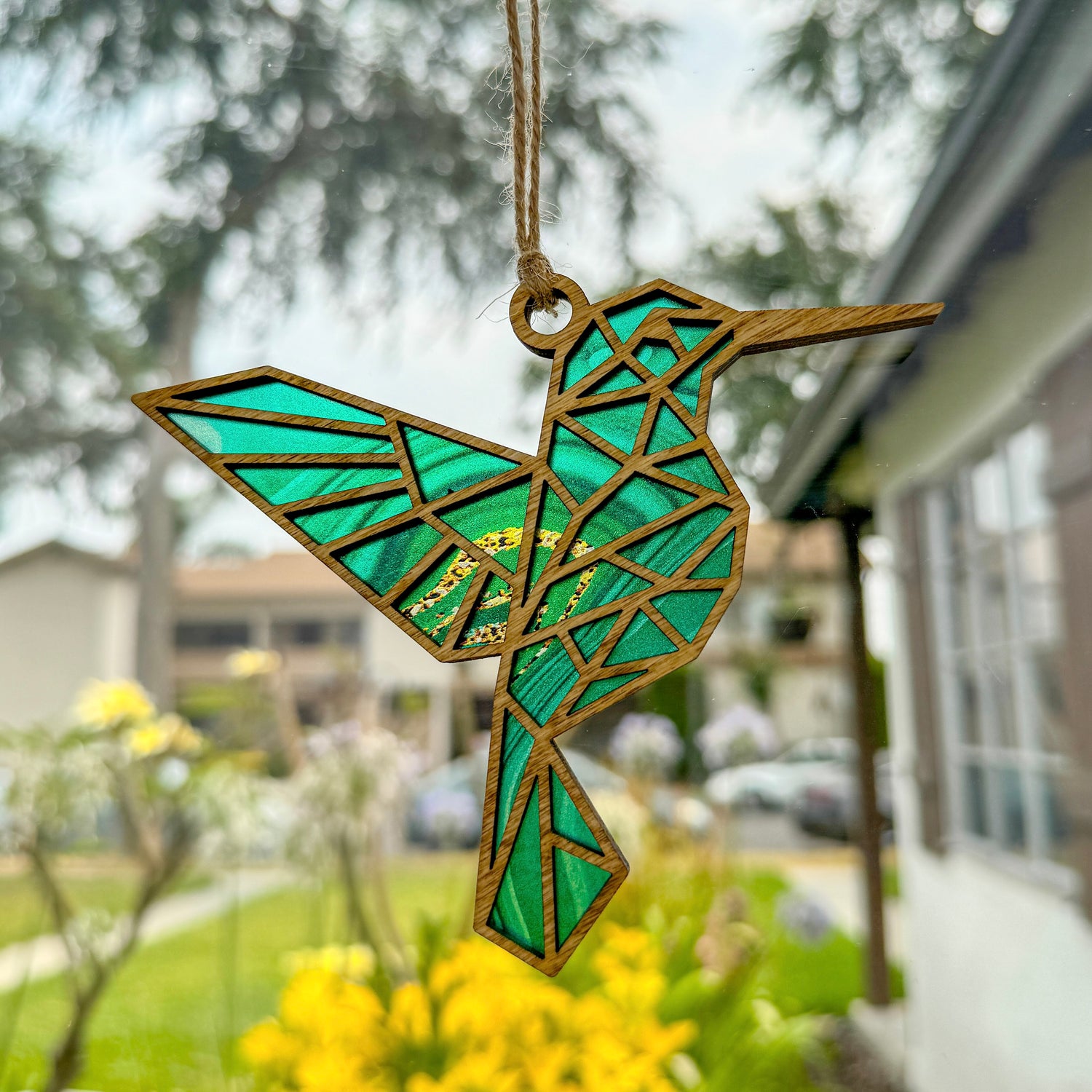 Geometric hummingbird suncatcher made from wood and acrylic hanging in window shown in the light stain option.