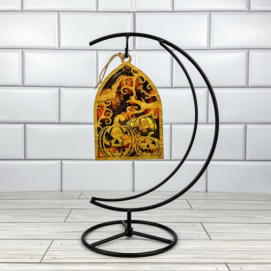 Jack-o'-lantern suncatcher made from wood and acrylic hanging on a metal stand in front of a white tiled wall.