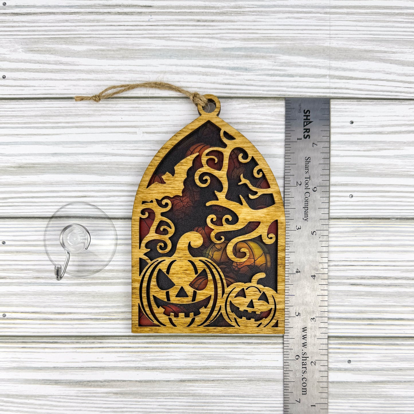 Jack-o'-lantern suncatcher made from wood and acrylic lying flat with a ruler showing the approximate height.