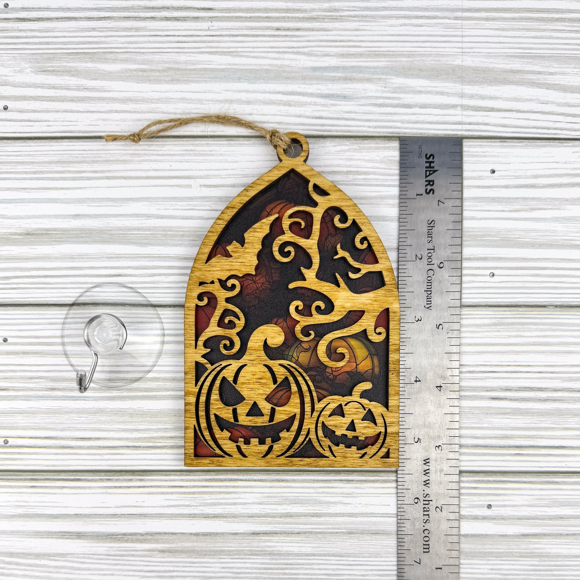 Jack-o'-lantern suncatcher made from wood and acrylic lying flat with a ruler showing the approximate height.