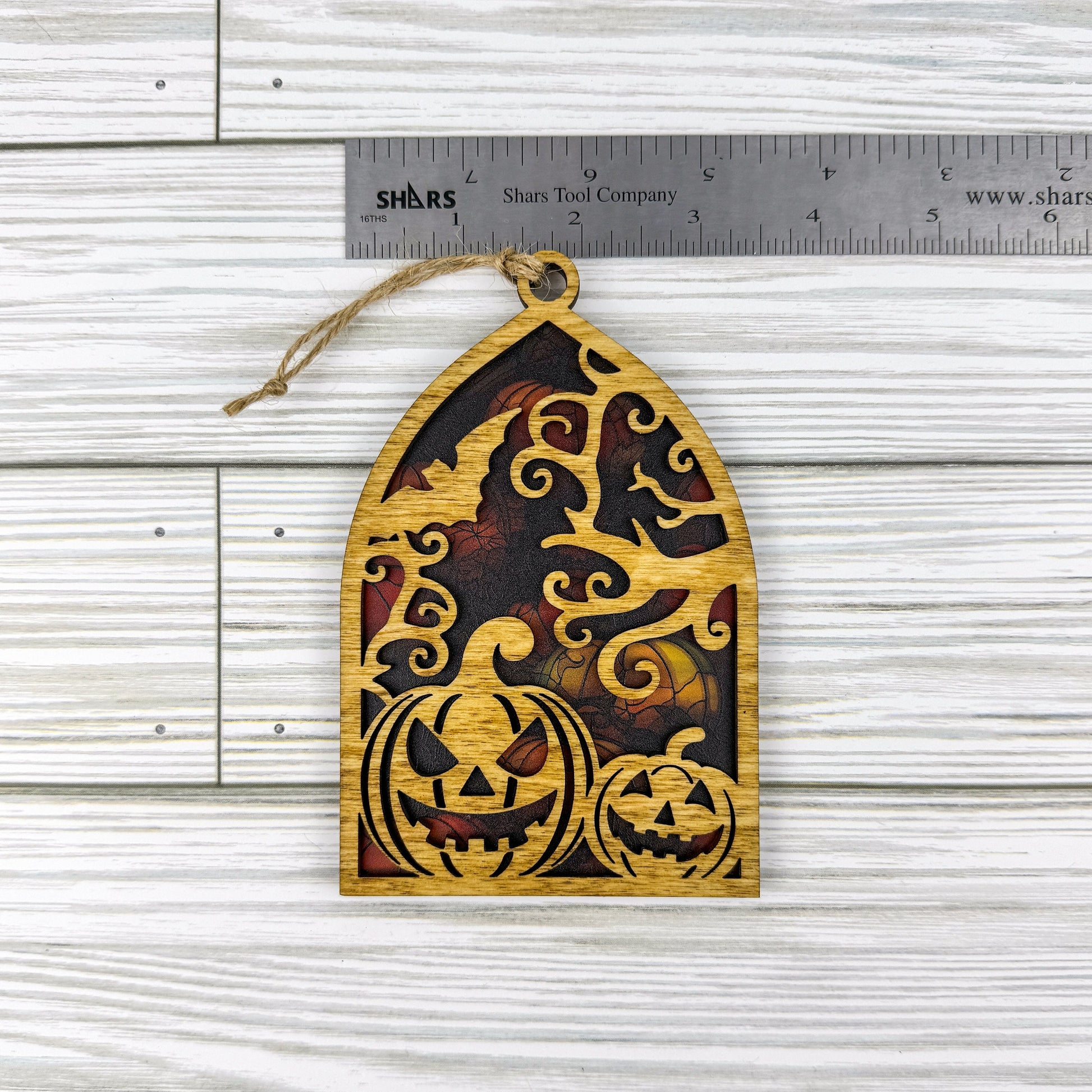 Jack-o'-lantern suncatcher made from wood and acrylic lying flat with a ruler showing the approximate width.