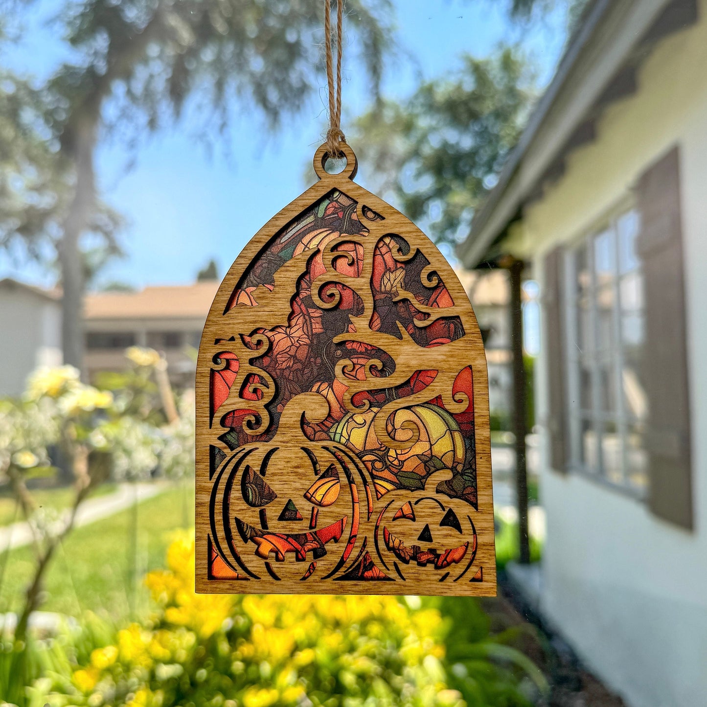 Jack-o'-lantern suncatcher made from wood and acrylic hanging in window.