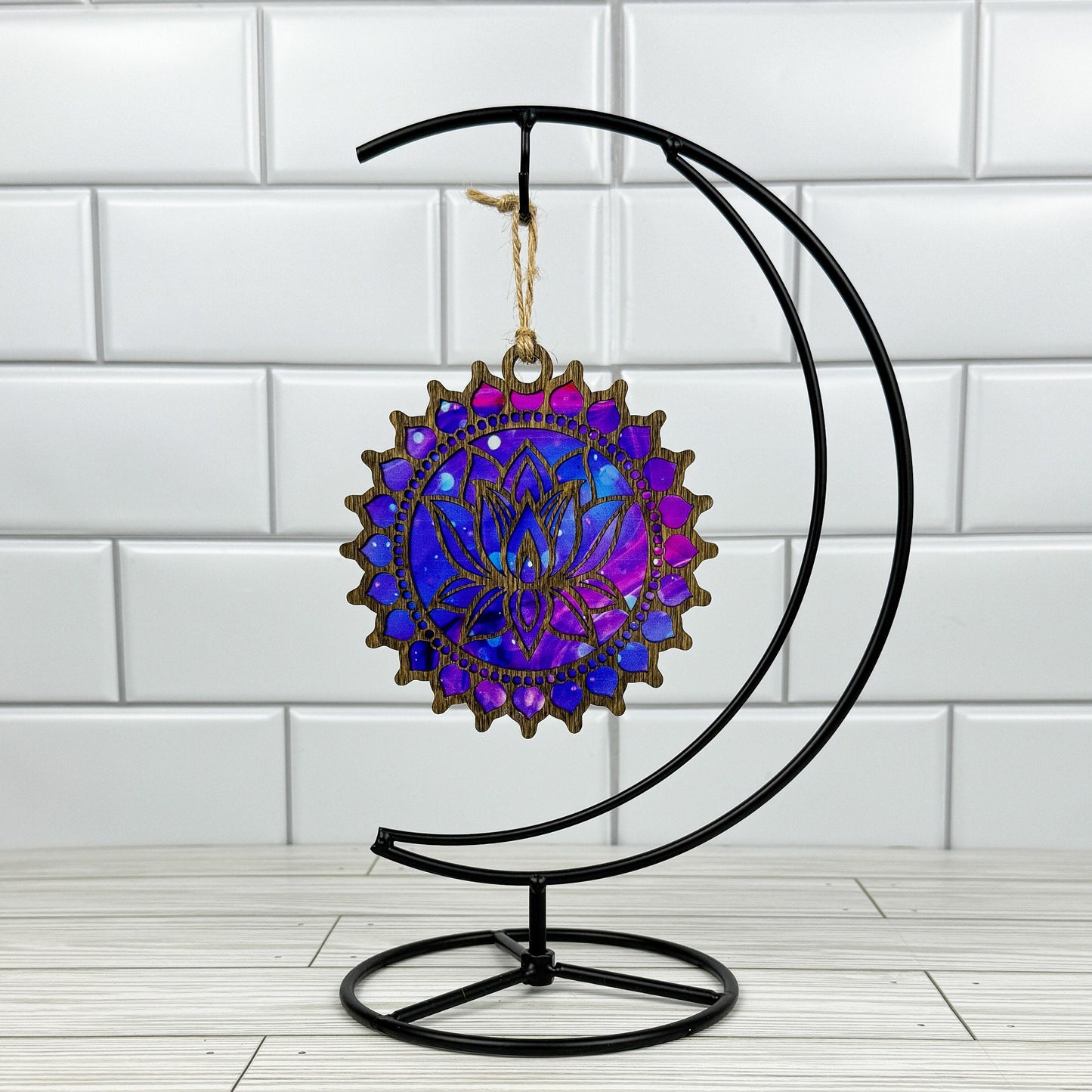Lotus flower suncatcher made from wood and acrylic hanging on a metal stand in front of a white tiled wall.