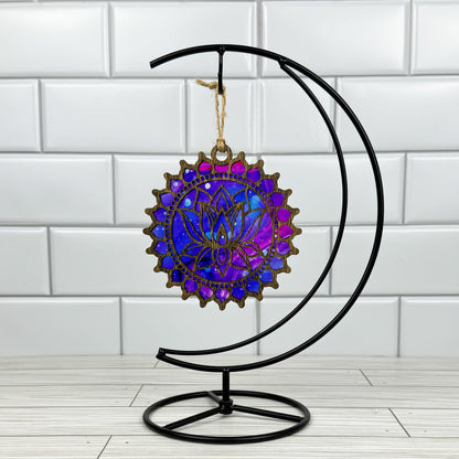 Lotus flower suncatcher made from wood and acrylic hanging on a metal stand in front of a white tiled wall.