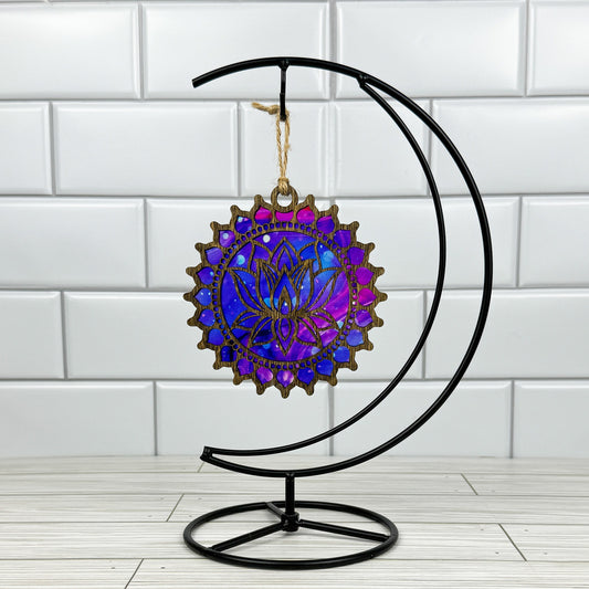 Lotus flower suncatcher made from wood and acrylic hanging on a metal stand in front of a white tiled wall.
