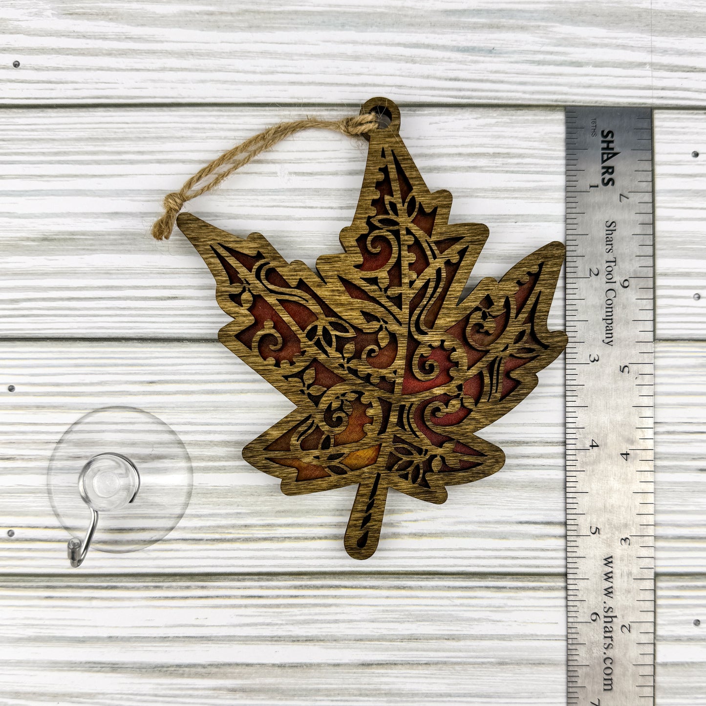 Maple leaf suncatcher made from wood and acrylic lying flat with a ruler showing the approximate height.