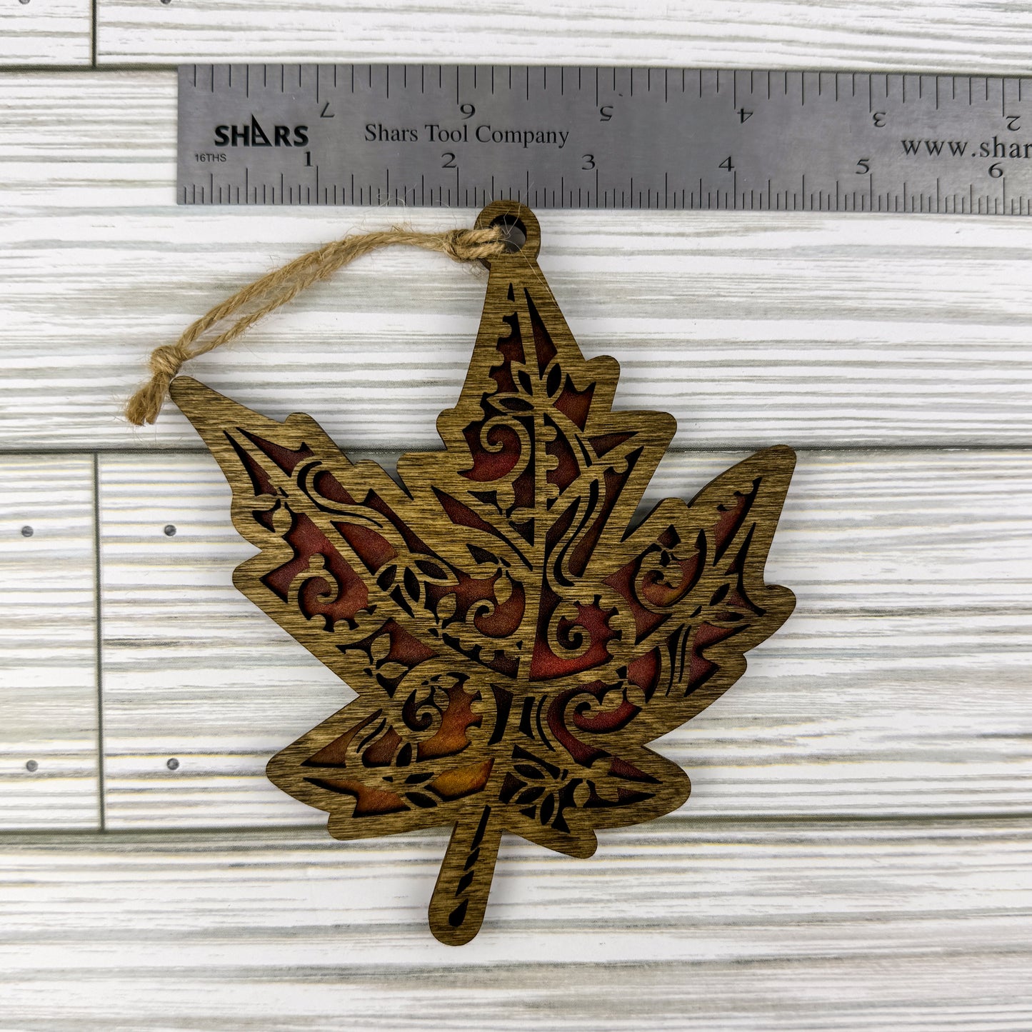 Maple leaf suncatcher made from wood and acrylic lying flat with a ruler showing the approximate width.
