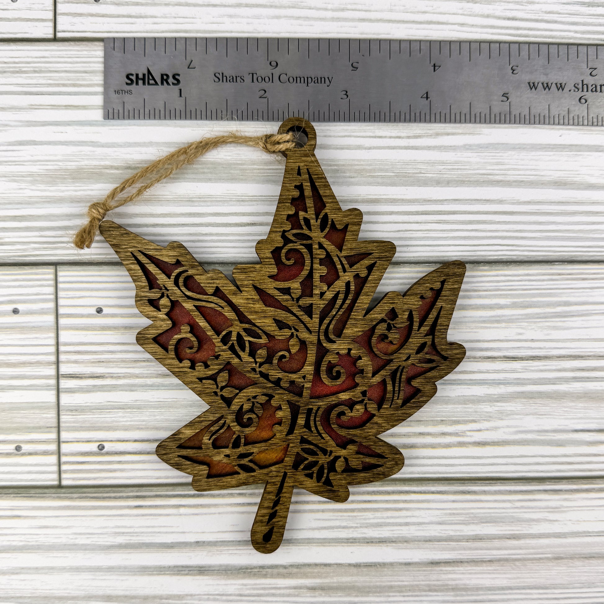 Maple leaf suncatcher made from wood and acrylic lying flat with a ruler showing the approximate width.