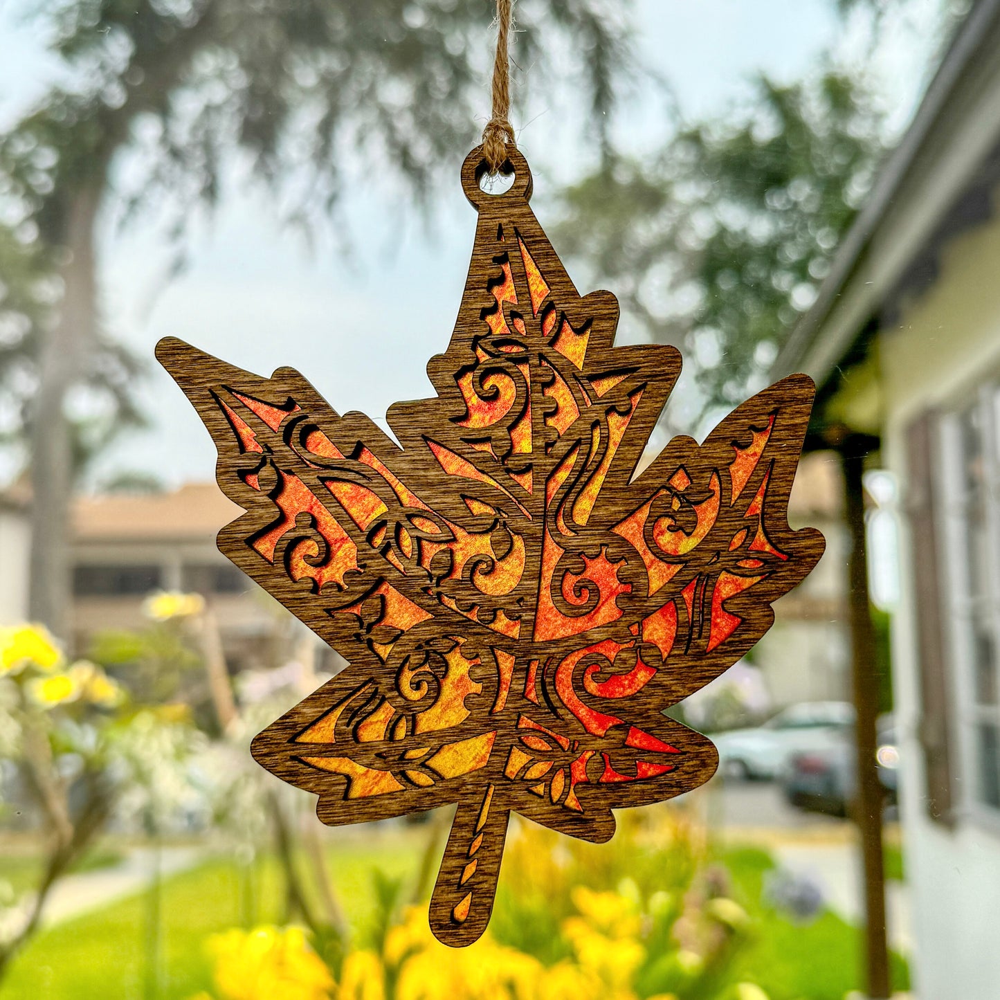 Maple leaf suncatcher made from wood and acrylic hanging in window.