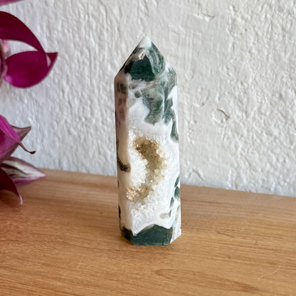 Crystal tower with green and white patterns on a wooden surface with a blurred background