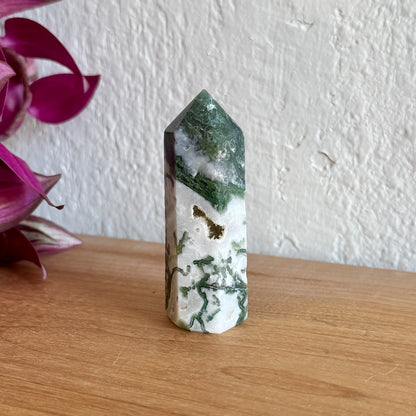 Moss agate crystal tower on a wooden surface with pink flowers in the background