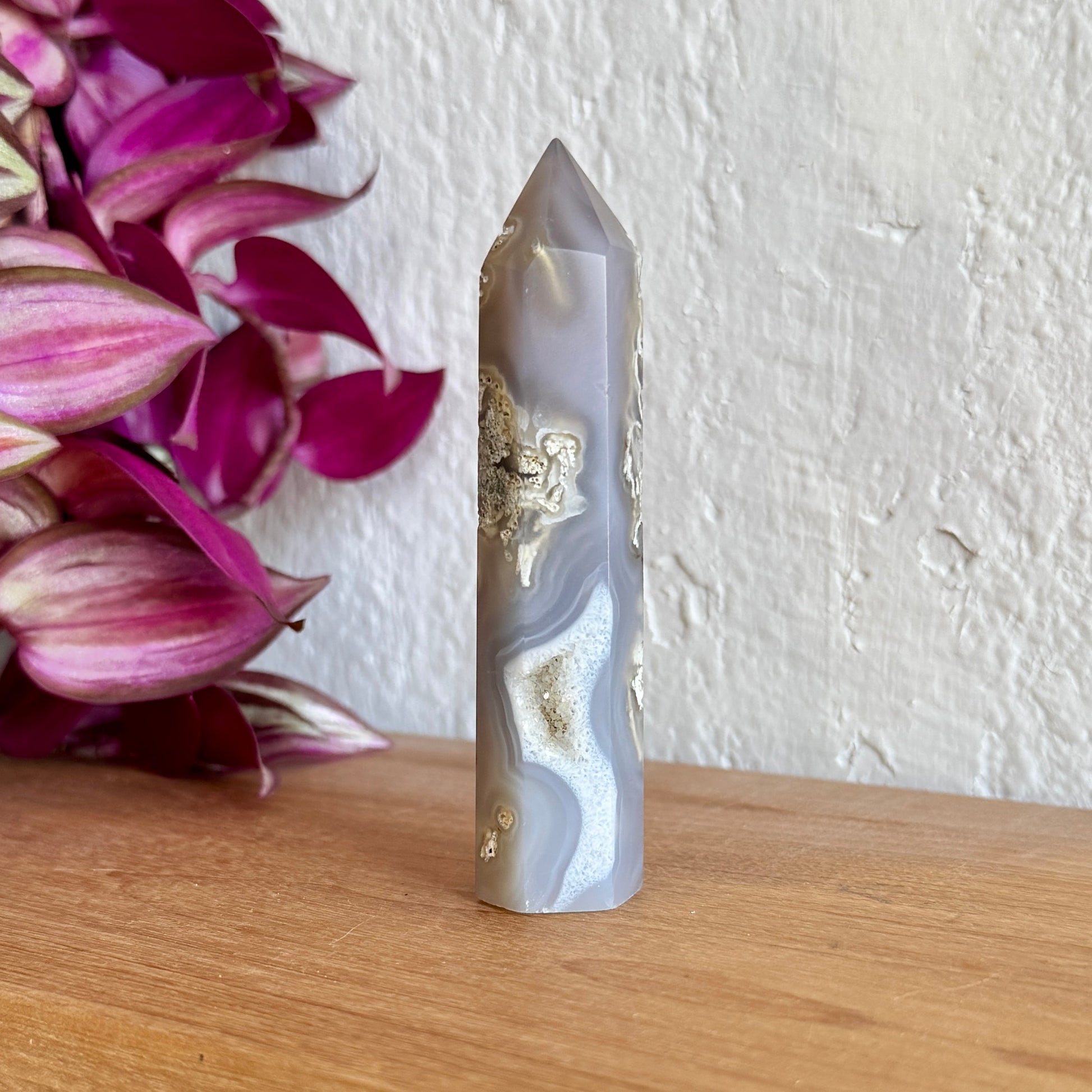 One moss agate crystal tower on a wooden surface with a white wall background
