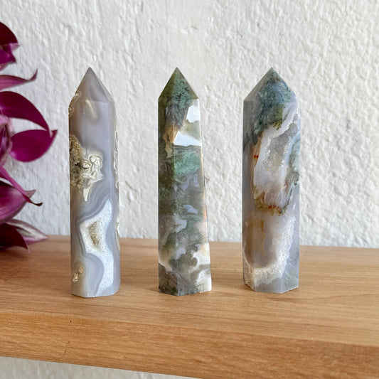 Three moss agate crystal towers on a wooden surface with a white wall background