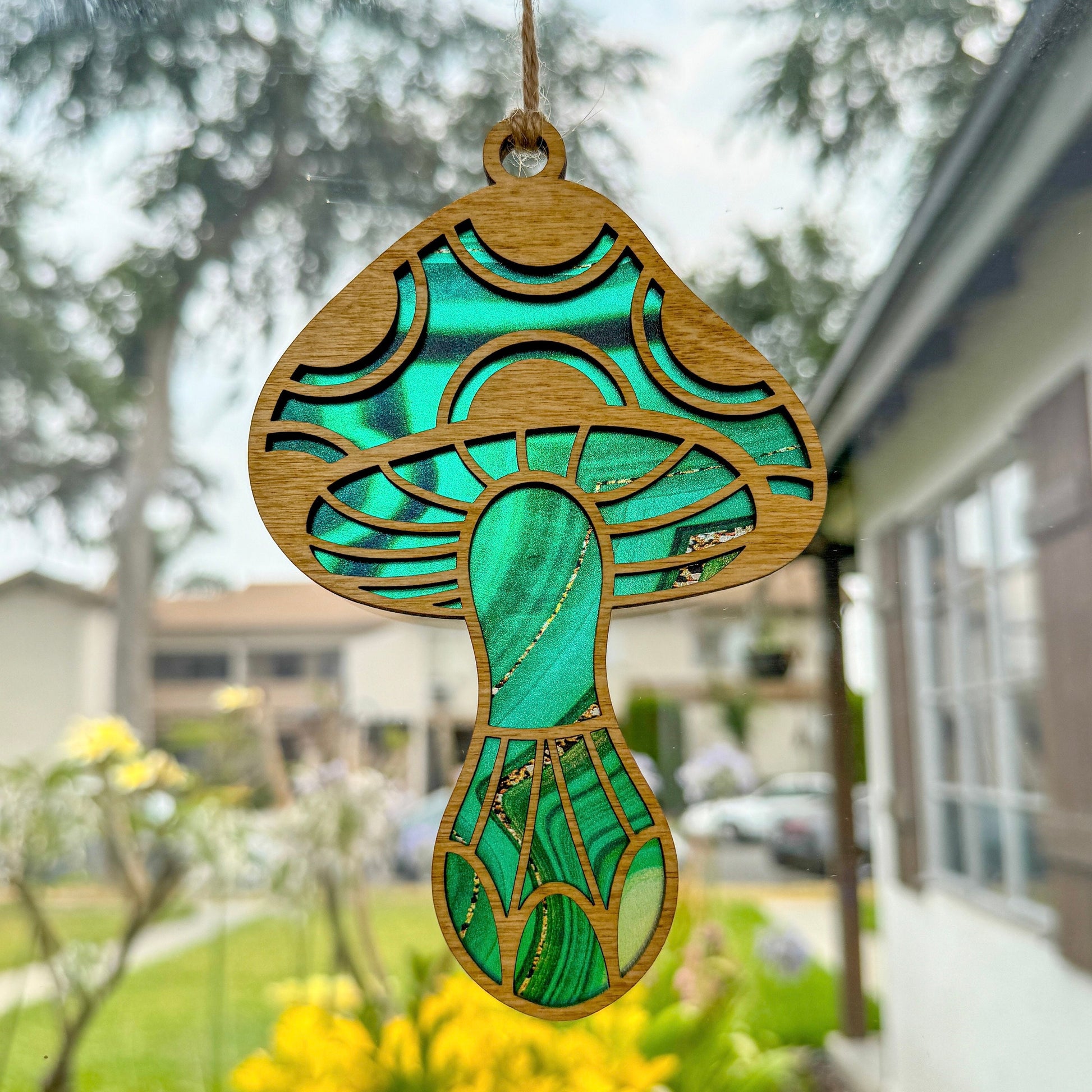 Mushroom suncatcher made from wood and acrylic with a green pattern hanging in window 