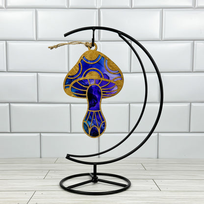 Mushroom suncatcher made from wood and acrylic shown in the blue and purple option hanging on a metal stand in front of a white tiled wall.