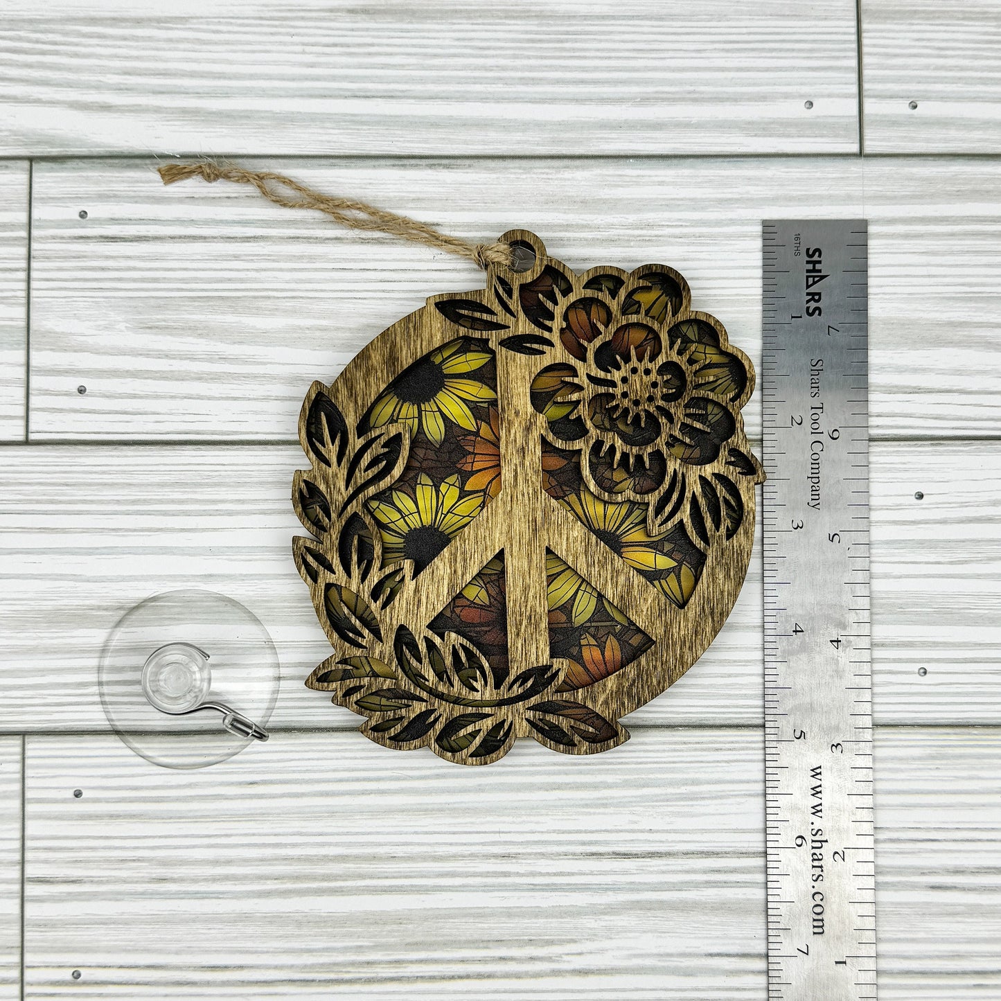 Wooden peace symbol suncatcher with floral design next to a ruler showing approximate height on a wooden surface