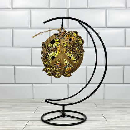Floral peace sign suncatcher made from dark stained wood and acrylic hanging on a metal stand in front of a white tiled wall.