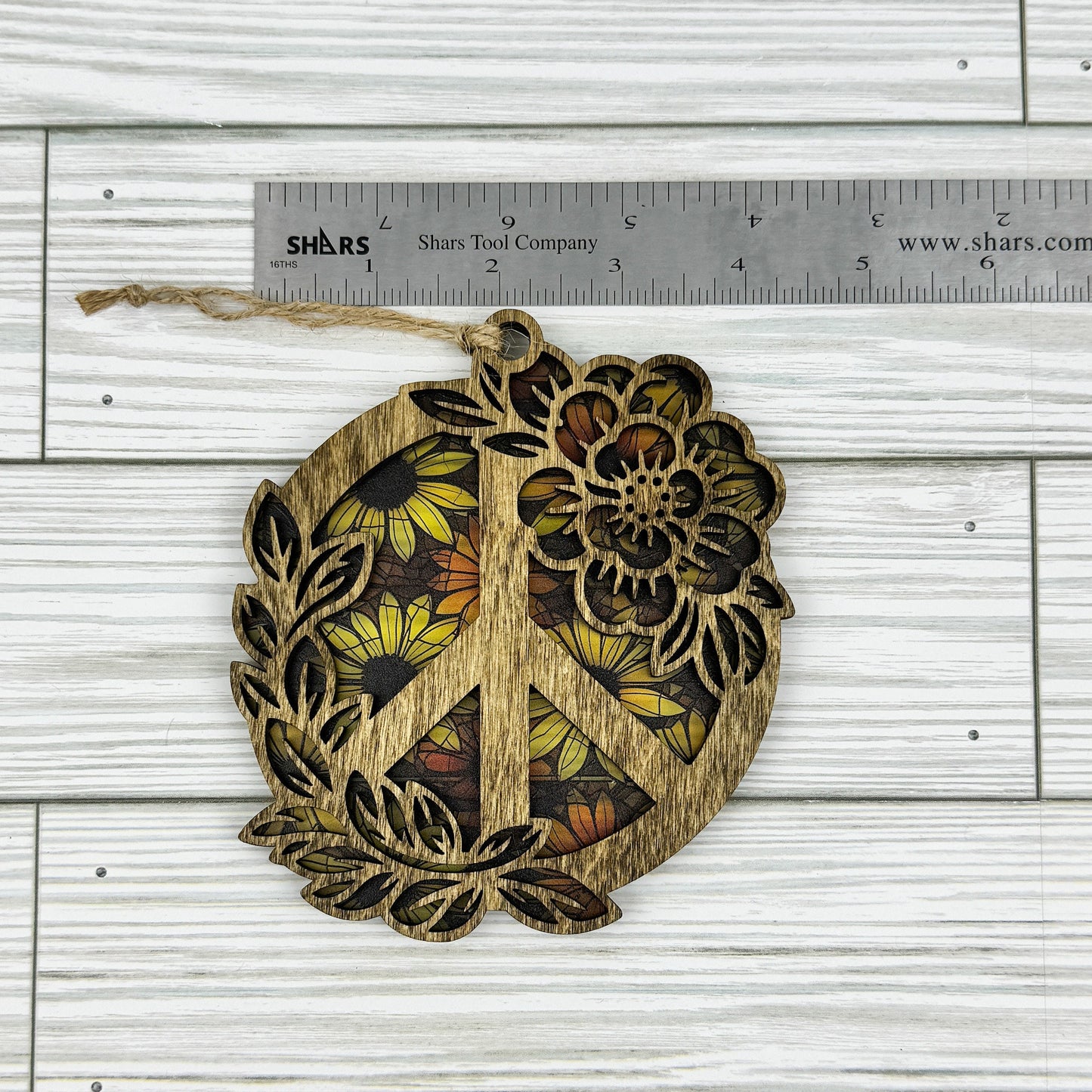 Wooden peace symbol suncatcher with floral design next to a ruler showing approximate width on a wooden surface